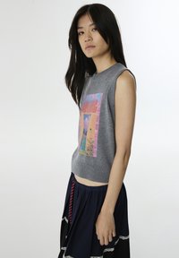 Graues gestricktes, ärmelloses Crop-Top mit einem bunten Grafikdruck, kombiniert mit einem marineblauen Rock mit Spitze und Kordelzug.