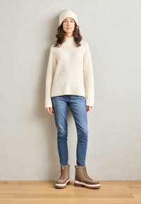 Suéter de canalé crema, vaqueros azules y botas de tobillo aisladas marrones con suelos blancos. Todos los artículos tienen una textura suave, creando un look cohesivo.