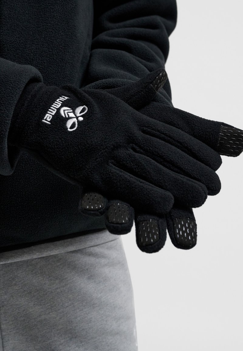 Svarta fleecehandskar med texturerat svart grepp på fingertopparna, med en vit logotyp på handleden. Mjukt material, ergonomisk design.