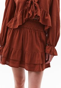 Roestkleurige twee-delige outfit met een ruffled crop top met een strik aan de voorkant en een high-waisted rok met gelaagde ruffles en een smocktail.