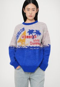 Šviesiai pilkas megztinis su mėlynais akcentais, su tropiniais raštais ir tekstu. Laisvas kirpimas, su įrengtu apvaliu kaklu ir rankovėmis.