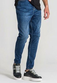 Niebieskie dżinsy o dopasowanym kroju z pięcioma kieszeniami, zestawione z czarnymi sneakersami z białymi sznurówkami i fakturowaną cholewką.