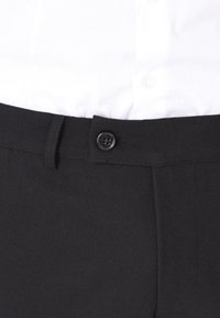 Pantaloni neri in tessuto con chiusura a bottone, tasca frontale singola e texture morbida, abbinati a una camicia bianca.