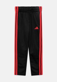 Schwarze Sporthose mit roten Streifen an den Seiten, aus weichem Stoff, mit einem elastischen Bund und einem Adidas-Logo am linken Bein.