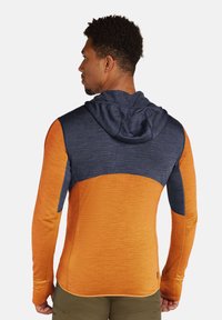 Hoodie met lange mouwen in een oranje kleur en een marineblauwe bovenkant. De stof is glad met een naad langs de schouder.