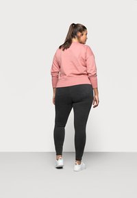 Light pink sweatshirt with ribbed cuffs and hem, paired with dark gray leggings. Model wears white sneakers. Focus on back view.