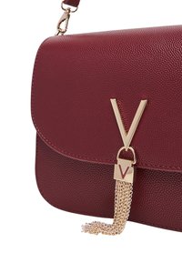 Borsa a mano in pelle bordeaux con una texture liscia, dotata di un logo "V" dorato e un accento con frangia a catena. Design compatto rettangolare.