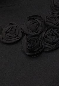 Μαύρο ύφασμα με πέντε ραμμένα μαύρα υφασμάτινα τριαντάφυλλα τοποθετημένα κοντά το ένα στο άλλο σε μια σειρά.