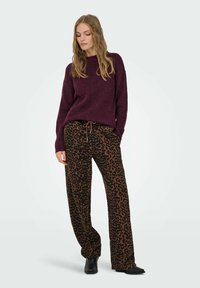 Bordeaux strikket sweater med lange ærmer, parret med brune leopardmønstrede vide bukser. Sorte ankelstøvler fuldender outfittet.
