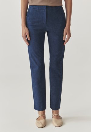 Tmavě modré kalhoty na míru se hladkým, lehkým materiálem. Mají standardní pas a rovný, slim fit až ke kotníkům.