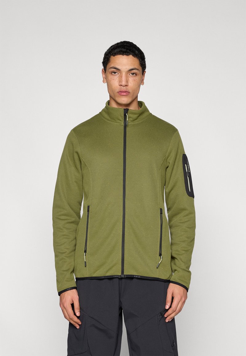 Φόρμα με φερμουάρ σε ελιά πράσινο χρώμα με ψηλό γιακά, υφή υφάσματος, τσέπες με μαύρο φερμουάρ και μαύρη λεπτομέρεια στο μανίκι.