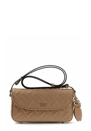 Sac bandoulière matelassé beige avec sangle noire, logo en métal doré "GUESS EST 1981" et breloque dorée avec des pompons sur fond blanc.