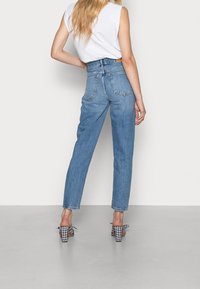 Höga blå jeans i denim med rak ben-design och bakfickor, kombinerat med rutiga klackskor.