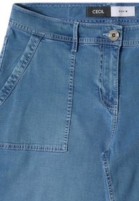 Blue denim jeans with front pockets, belt loops, a metal button closure, and a visible label reading "CECIL DENIM" inside the waistband.