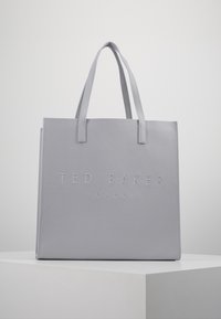 Jasnoszara torba tote Ted Baker London z podwójnymi uchwytami, stojąca na białym piedestale na tle gładkiego szarego tła.