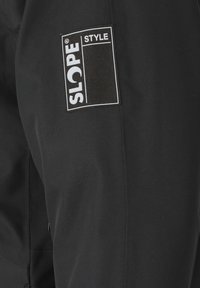 Mustat hiihtohousut, joissa on sileä pinta, ja joissa on valkoinen "SLOPE STYLE" -logopatchi sivussa. Yksinkertainen, toiminnallinen muotoilu.