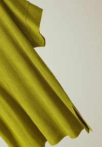 Top de punto texturizado en verde lima con mangas cortas, que presenta un detalle de abertura lateral y un diseño de corte holgado.