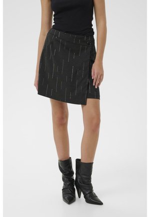 Black fabric mini skirt with vertical metallic accents, wrap design, and a side button closure. Worn with black pointed-toe heeled boots.