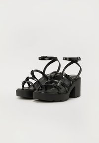 Black platform sandals with multiple narrow straps, a block heel, and ankle buckle closures. Smooth, shiny material with a sleek design.