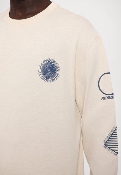 Beige long-sleeve sweatshirt with round neckline. Features blue graphic designs on the chest and sleeve, made from soft, textured fabric.