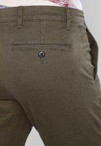 Pantalon vert olive, en mélange de coton, avec une poche arrière dotée d'un seul bouton noir, des détails de couture subtils et une coupe droite.