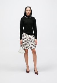 Black knit sweater, floral print skirt in cream with purple accents, white handbag, and burgundy pointed-toe heels, model standing upright.