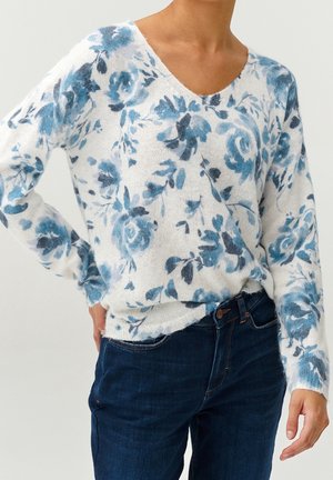 Pull fleuri présentant des nuances de bleu sur un fond blanc, fabriqué en matière douce et texturée avec un col en V et une coupe décontractée.