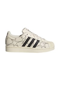 Baskets en cuir blanc avec motifs d'étoiles noires, comportant trois rayures noires, des lacets plats et un embout en caoutchouc texturé.