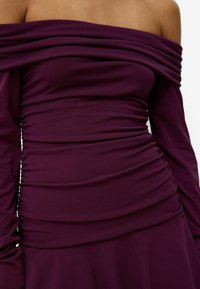 Lila av-axeln klänning med draperat tyg, långa ärmar och samlade detaljer längs bodice, tillverkad av stretchigt material.