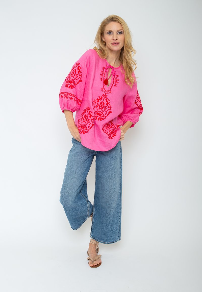 Rosa Leinen-Bluse mit roter floralem Stickerei, lockere Passform, 3/4-Ärmel, kombiniert mit weit geschnittenen Jeans und Sandalen.