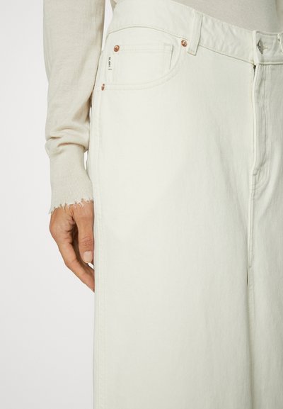 Witte denim jeans met koperen hardware, een label op de voorkant van de broekzak en een licht uitgerafelde zoom. De stof heeft een gladde, stevige textuur.