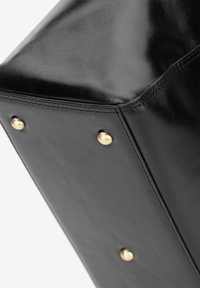 Zwarte leren tas hoek met een gladde textuur, voorzien van gouden metallic hardware accenten en zichtbare stiksels op de randen.