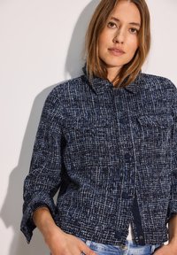 Giacca in tweed navy con un motivo testurizzato, chiusura a bottoni e due tasche sul petto. Presenta un colletto e maniche a tre quarti.