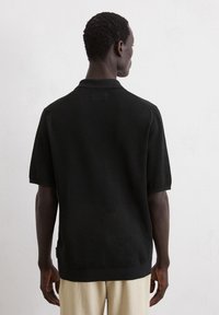 Polo noir à manches courtes en tissu tricoté texturé, avec un col et des poignets côtelés, et un ourlet droit, vu de l'arrière.