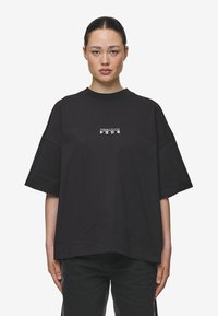 Zwarte katoenen oversized t-shirt met een ronde hals en korte mouwen. De voorkant heeft een minimalistisch wit tekstlogo. Soepele textuur en een relaxte pasvorm.