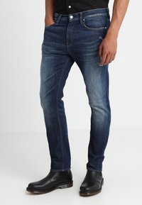 Ciemnoniebieskie dżinsy o dopasowanym kroju, z przetarciami na udach, pięcioma kieszeniami oraz kontrastowymi detalami w szwach. Noszone z czarnymi botkami.