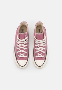 Růžové vysoké tenisky z plátna s bílými tkaničkami, gumovou špičkou a kontrastním černým lemem podél podrážky. Klasické designové prvky.