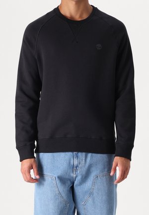 Zwarte sweatshirt met raglanmouwen, getextureerde ronde hals en geribbelde zoom. Bevat een klein logo op de borst. Gecombineerd met lichtblauwe jeans.