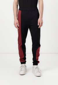 Zwarte en bordeaux joggers met een elastische tailleband, opgerolde enkels, zijzakken en een kleurblokontwerp. Zachte stof textuur.