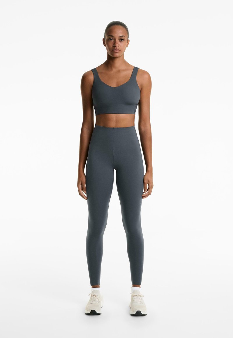 Szürke sportmelltartó és magas derekú leggings rugalmas anyagból. A dizájn v-nyakkivágással és varrás nélküli befejezéssel rendelkezik. Könnyű sportcipőkkel egészítve.