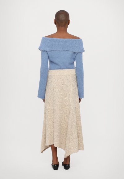 Light blue off-shoulder sweater made of soft material, paired with a cream, textured asymmetrical skirt. Black slip-on shoes complete the look.