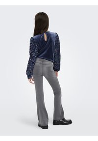 Top em veludo azul-marinho com mangas bufantes de lantejoulas e decote em gota nas costas; combinado com calças cinzentas justas e com folho e sapatos pretos robustos.