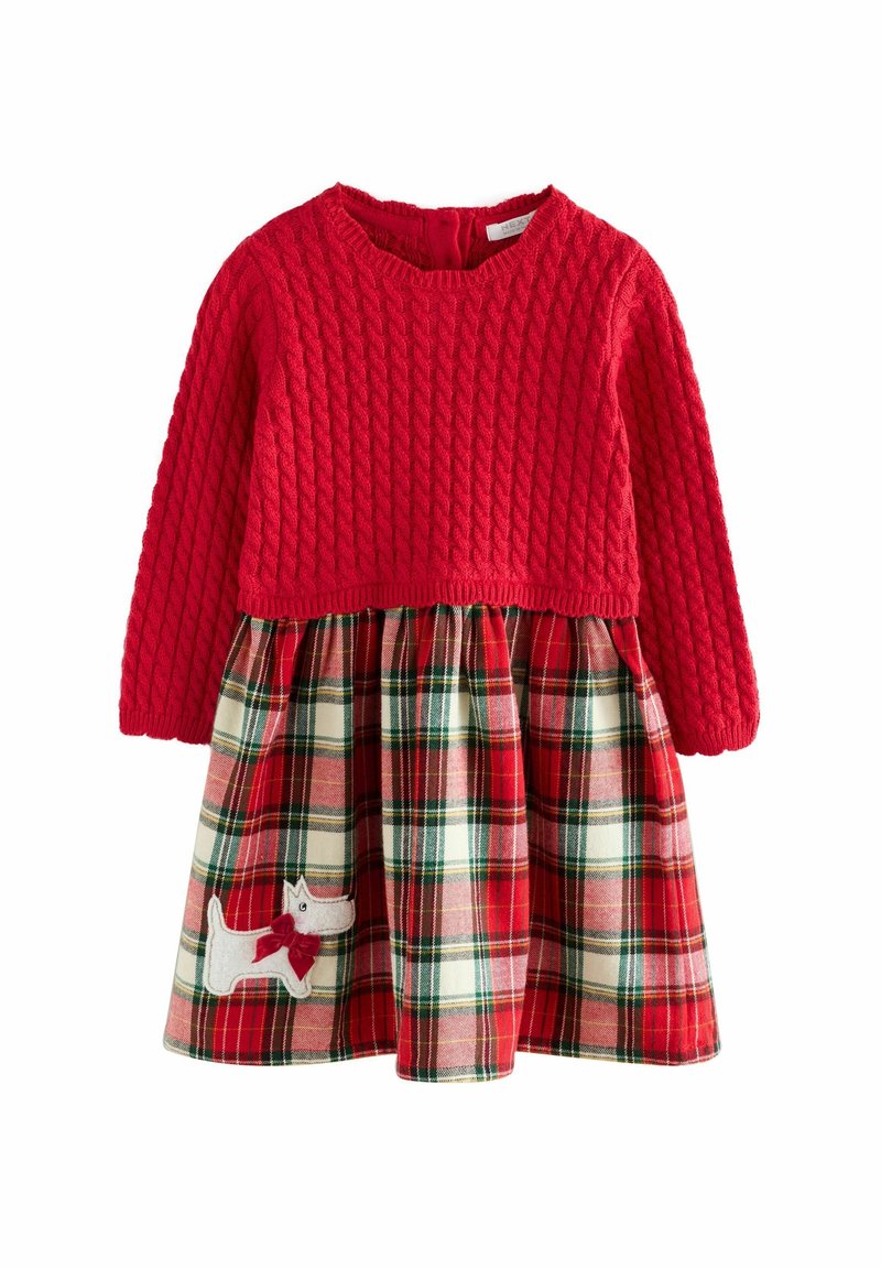 Haut rouge en maille à manches longues avec un motif torsadé, attaché à une jupe à carreaux rouge, verte et blanche, comportant un écusson chien blanc avec un nœud rouge.