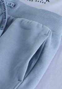 Světle modré tepláky s žebrovaným pasem a kapsami, s jemnou texturou a ležérním designem. Štítek uvádí "Ted Baker."