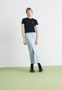 Schwarzes, figurbetontes T-Shirt, hellblaue Denim-Rock mit einem Schlitz vorne, getragen mit schwarzen, schnürbaren Kampfstiefeln. Einfaches, klar geschnittenes Design.