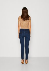 Tmavě modré skinny džíny vyrobené z denimu, s vysokým pasem a zadními kapsami. V kombinaci s texturovaným, světle hnědým tílkem bez rukávů.