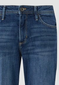 Ciemnoniebieskie jeansy z denimu o wysokim stanie, z klasycznym zapięciem na guzik, pięcioma kieszeniami i złotym przeszyciem wzdłuż szwów.