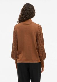 Pull marron avec un corps lisse et des manches bouffantes texturées arborant un motif en losange. Le col est côtelé et la coupe est décontractée.