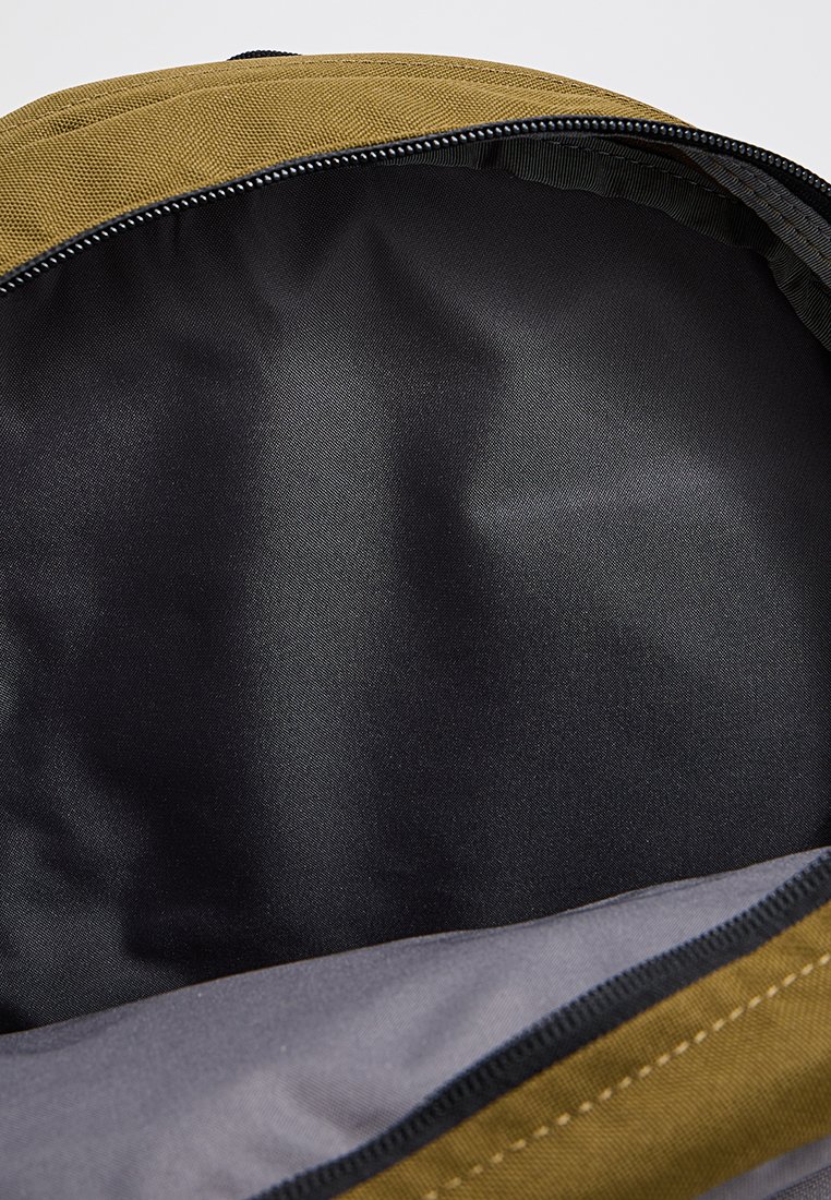 Innenraum eines olivgrünen Stoffrucksacks mit glattem schwarzen Futter und einem grauen Reißverschluss. Minimalistisches Design, geräumiges Fach für die Aufbewahrung.
