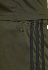 Olivgrüne Sportshorts mit schwarzen Seitenstreifen, mit dem schwarzen "AEROREADY"-Logo auf der Vorderseite, aus glattem, strukturiertem Stoff.